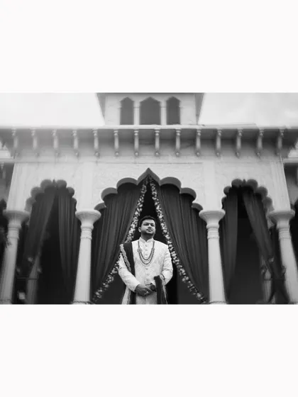 A powerful black and white shot of the groom standing in front of a grand, traditional building.