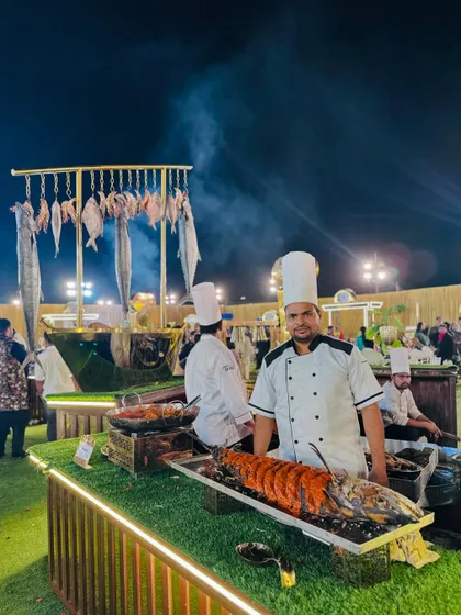 A chef at the seafood station, with a large grilled lobster and a backdrop of hanging fresh fish.