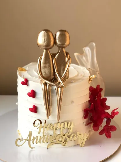A minimalist anniversary cake with an abstract golden couple topper and a pop of red.