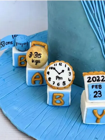 A closer look at the custom birth announcement toppers. Each block features a hand-painted detail, like the calendar, clock, and kettlebell, making it a unique and memorable part of a baby welcome cake.