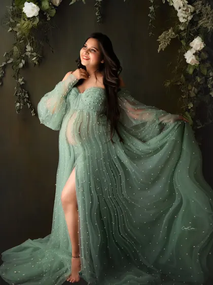 A joyful portrait of a mom-to-be in a flowing green gown, standing under a beautiful arch of white and green foliage.