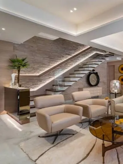 In this duplex living room, the staircase is a central design feature, with stone-textured walls and integrated lighting. The mix of modern furniture and natural elements creates a space that is both grand and welcoming.