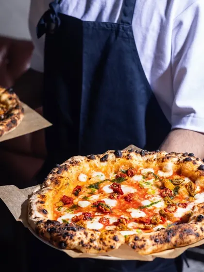Double the pizzas, double the love. A server holds two of my signature wood-fired pizzas, showcasing the beautiful, blistered crust and fresh toppings, ready to make someone's day.