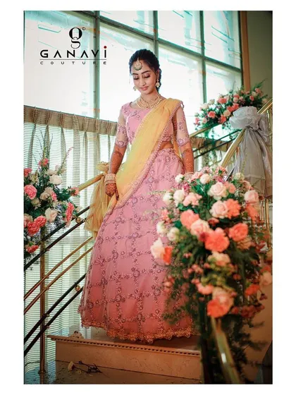 The bride-to-be descends a staircase in her custom pink engagement lehenga. This shot captures the beautiful flow and movement of the skirt, adorned with floral decorations that complement the outfit perfectly.