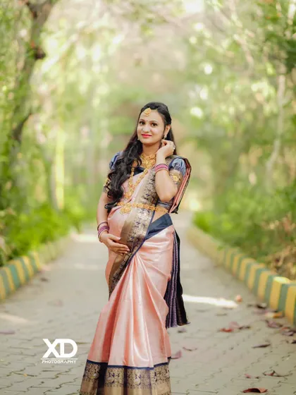 A classic solo maternity pose in a beautiful silk saree, captured on a tree-lined path.