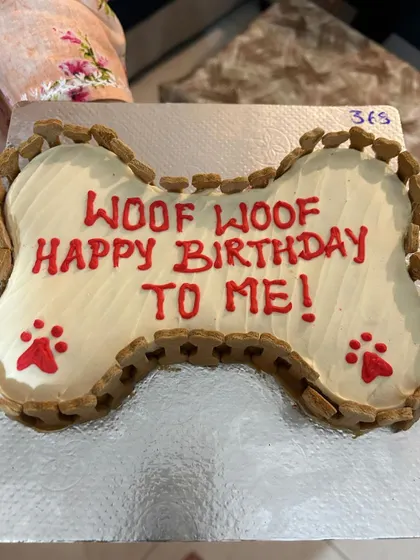 "Woof Woof Happy Birthday To Me!" This fun message is written on a classic bone-shaped cake, edged with crunchy baked biscuits.
