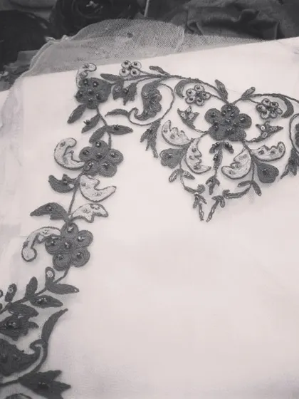 A work in progress. This black and white photo highlights the form and structure of a floral embroidery pattern being crafted on sheer fabric, showcasing the artistry before it becomes part of a finished garment.