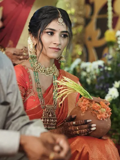 A beautiful bride holding a traditional pot during her wedding ceremony, wearing a stunning orange Kanjivaram saree.
