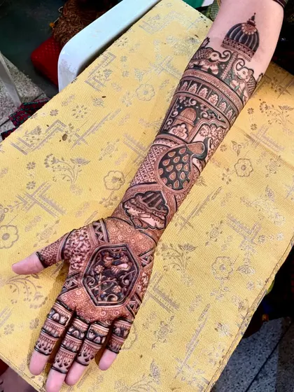 This bridal design is filled with intricate elements, including peacocks, elephants, and a central mandala, covering the arm from palm to elbow.