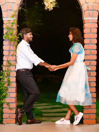 A romantic pose with the couple holding hands, framed by brick arches. The night setting adds a touch of intimacy.