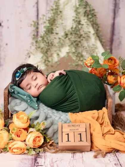 A sleeping baby girl wrapped in green, nestled in a wooden crate with orange floral decorations.