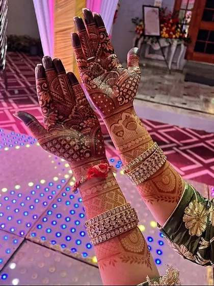 A gorgeous photo of a client's mehndi stain at an event. The deep color of the henna stands out beautifully against the festive lights and her sparkling bangles.