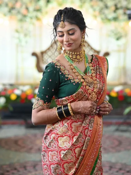 A stunning bride in her complete Muhurtham look, wearing a red and green saree with a custom heavy-work green blouse.