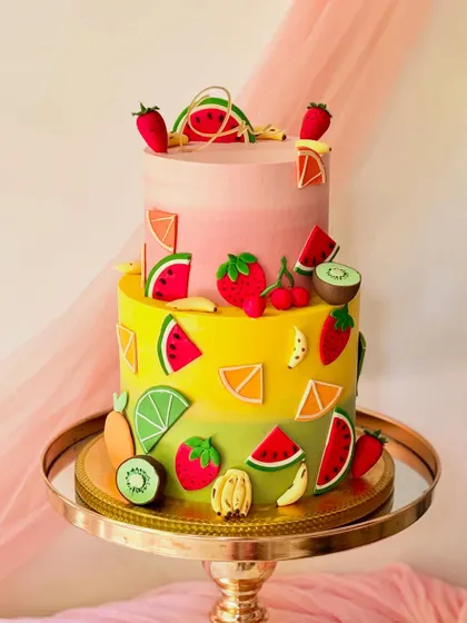 Another vibrant fruit-themed cake. This two-tiered design is covered in a variety of colourful, handcrafted fondant fruits like strawberries, kiwis, and oranges.
