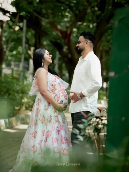 A beautiful moment shared between partners during an outdoor maternity shoot. The soft floral dress and the gentle sunlight create a dreamy, romantic feel.