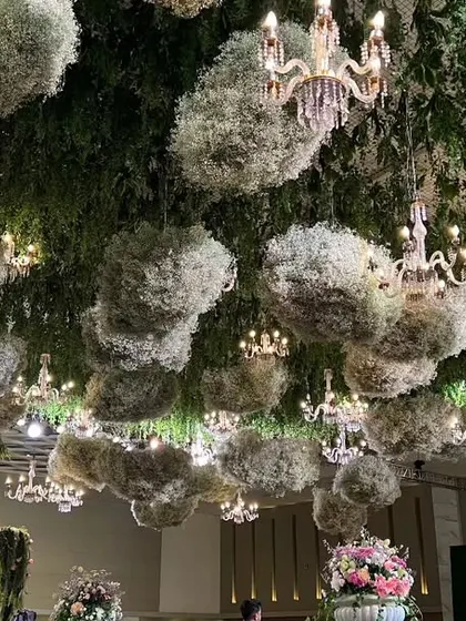A view of the ceiling, adorned with floating clouds of baby's breath and numerous chandeliers, creating a dreamy, ethereal sky inside the venue.