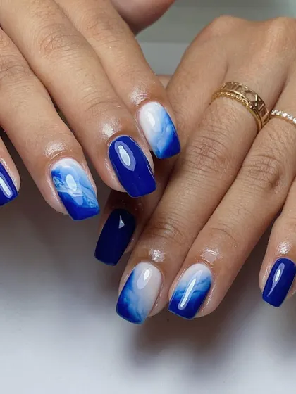 Ocean-inspired nails with a deep blue base and a white "seafoam" or marble effect.