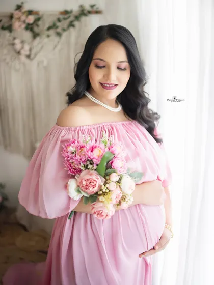 A close-up portrait of a mother-to-be holding a bouquet of pink flowers. This soft and feminine shot perfectly captures the "blooming" stage of pregnancy.