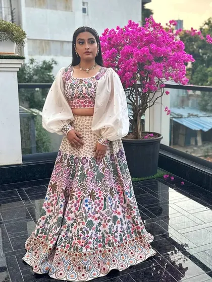 A full view of the soft pink raw silk lehenga, showcasing the intricate, dense embroidery that covers the skirt. The organza puff-sleeve blouse creates a beautiful contrast in texture and silhouette.