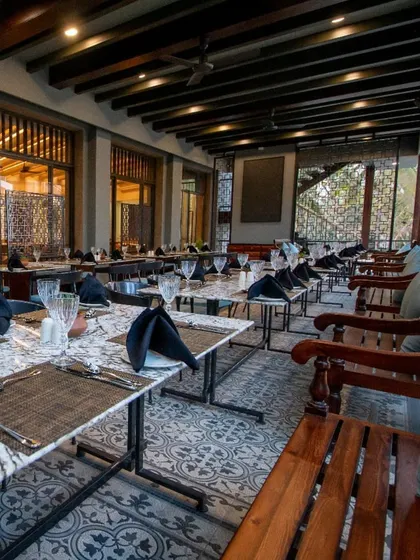Another perspective of the restaurant's outdoor section, highlighting the traditional wooden benches and intricate window details. The design blends classic Indian architectural elements with modern restaurant functionality.