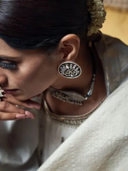 A detailed shot focusing on handcrafted ethnic jewelry. The lighting is carefully controlled to accentuate the craftsmanship of the silver earring and the model's contemplative expression.