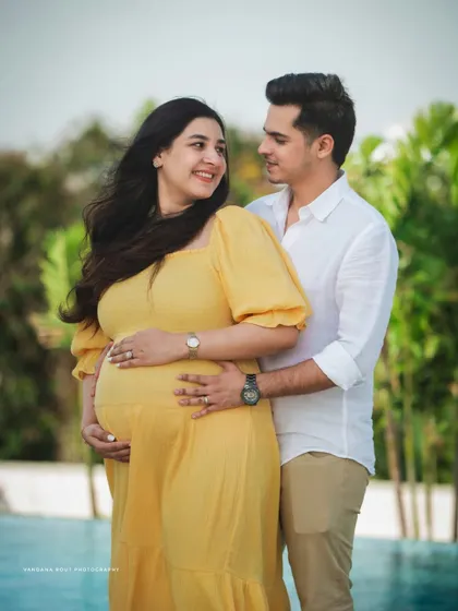 A classic couple's maternity pose by the pool, with both partners gently holding the baby bump. The lush green background adds a tropical feel to this Bangalore photoshoot.