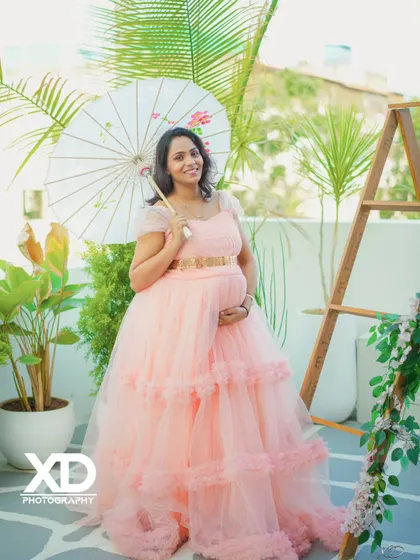 An elegant solo portrait of the mother-to-be in a peach gown, holding a paper umbrella in a bright studio setting.