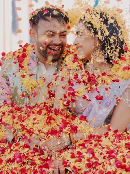 A joyful, candid shot of the couple laughing as they are showered with flower petals during their Haldi.