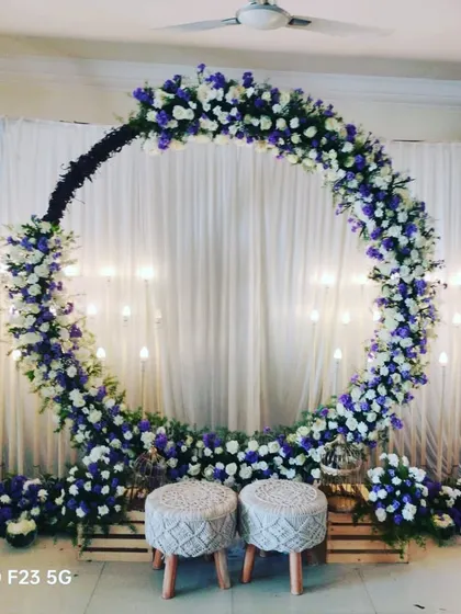 A beautiful baby shower decoration featuring a full floral ring of white and purple flowers against a curtain backdrop. The setup is simple, elegant, and perfect for celebrating a new arrival.