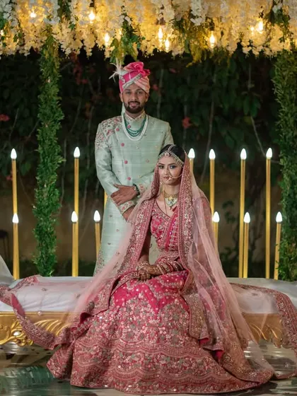 A regal, formal portrait of the couple in their stunning pink and mint green wedding outfits, set against a dramatically lit backdrop.