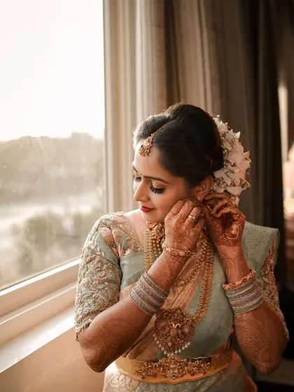 A bride adjusts her earring while standing by a window, bathed in natural light. This getting-ready shot captures a classic, contemplative bridal moment.