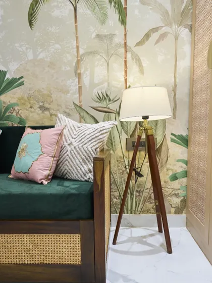 A cozy corner in a bedroom featuring a tropical-themed wallpaper, a velvet green divan, and a tripod floor lamp. It’s all about creating a soft, relaxing mood.