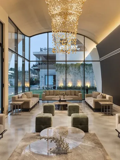 The interior of "The Rising Wave" outhouse is designed for grand entertaining. The arched ceiling and full-height glass walls create a voluminous, light-filled space, seen here set up for an evening event with a stunning view of the gardens.