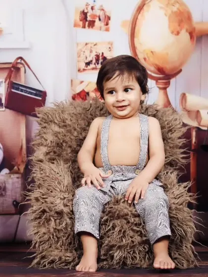 A relaxed toddler poses in a miniature armchair during his vintage-themed session.