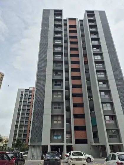 A ground-level view of the completed Adani Amogha towers in Ahmedabad. The facade design incorporates a mix of materials, including textured concrete and brick-colored accents, to create visual interest and texture.