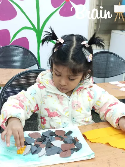 A moment of deep concentration as a young student carefully places pieces of paper for her collage. Art provides a wonderful opportunity for children to practice focus in a calm setting.