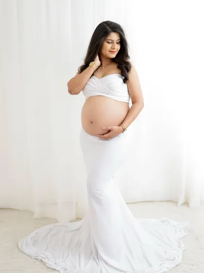 A minimalist and elegant portrait. The mom-to-be wears a white two-piece outfit that beautifully showcases her baby bump against a clean background.