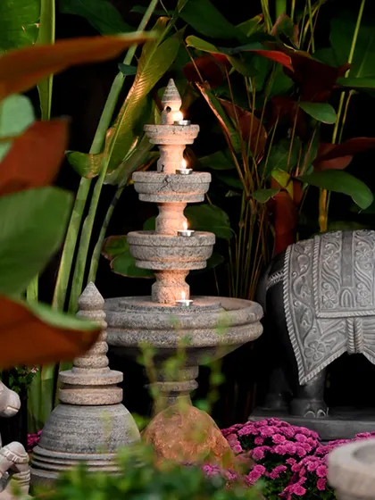 A tiered stone temple lamp illuminated with candles, set amidst lush greenery and an elephant statue. This scene captures the magical ambiance we create for festive celebrations like Diwali.