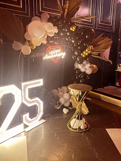 A sophisticated 25th-anniversary party with a black and white balloon arch, dried palm leaves, and a light-up number '25'.