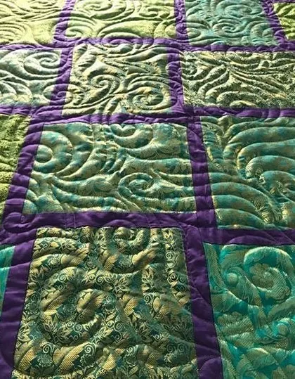 A close-up of a quilt with a rich, textured, custom quilting pattern in green and purple.