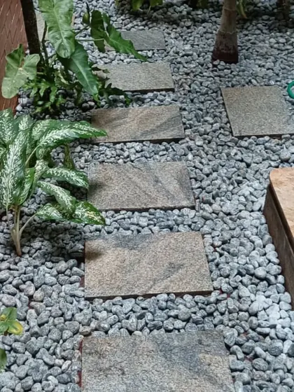 This path uses grey pebbles and rectangular stone pavers, creating a modern and textured walkway next to a brick wall.