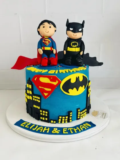 A super cake for a twin's birthday, featuring handcrafted fondant figures of both Superman and Batman.