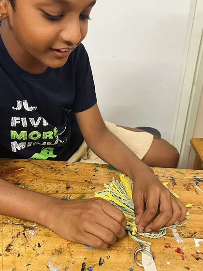 The smile of a creator! This student is enjoying the process of making his own macrame keychain, a project that boosts both creativity and confidence.