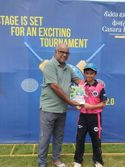 A young player receives a trophy for his performance in front of the tournament banner.