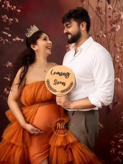 A fun pregnancy announcement photo. The couple smiles at each other while the partner holds a "Coming Soon" sign, adding a playful touch to their maternity shoot.