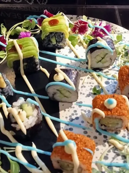 An example of our creative sushi plating. Here, assorted sushi rolls are arranged on a dark platter and garnished with colorful sauces and edible flowers, turning a classic dish into a modern culinary creation.