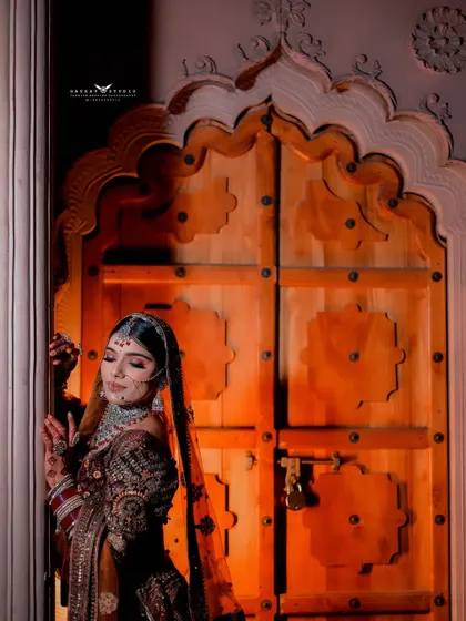 A moody and artistic shot of the bride by the ornate wooden door. The play of light and shadow creates a dramatic effect, highlighting her silhouette and the texture of her outfit.