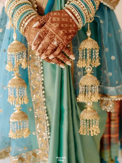 A close-up shot of the bride's hands, adorned with intricate henna and traditional kalire, resting on her stunning turquoise saree.