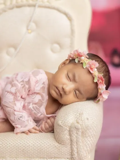 A close-up of the newborn princess, wearing a delicate floral crown and sleeping peacefully on her throne.
