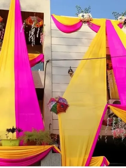 A bright and sunny view of a house decorated with long pink and yellow drapes for a daytime wedding event.